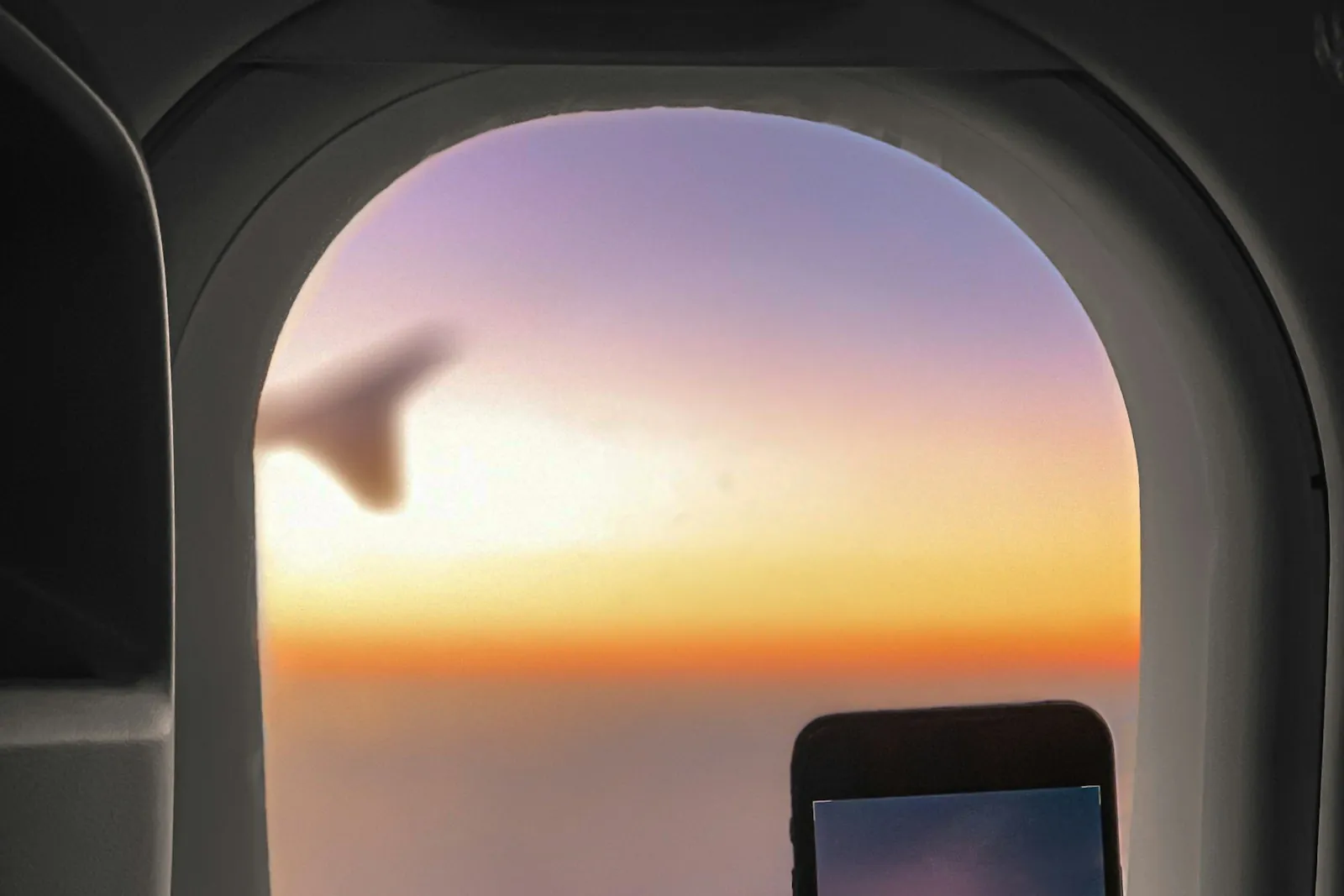 Korea eSIM before arrival — a traveler's phone at an airplane window at sunset before landing in Korea