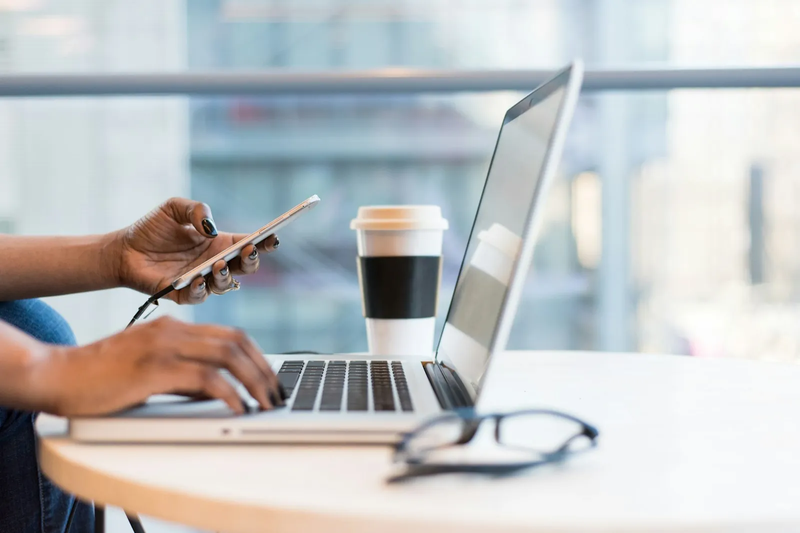 Person using a smartphone next to a laptop and coffee in a cafe, illustrating realistic Korea unlimited data eSIM versus fixed data plan choices