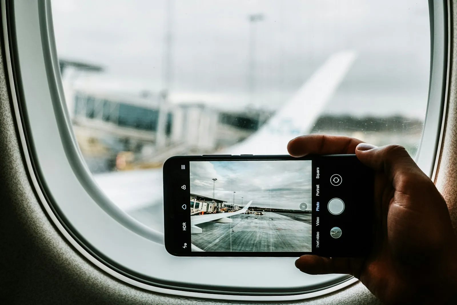 Traveler photographing a plane wing through an airplane window with a smartphone, illustrating a Korea Japan eSIM switching data on arrival for a combined trip